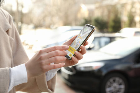 Photo of a woman ordering taxi with smartphone on city street, closeup